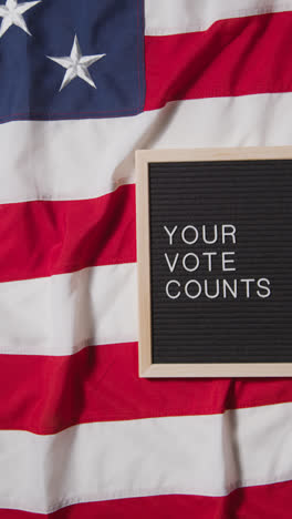 Vertical-Video-Of-Sign-Reading-Your-Vote-Counts-Lying-On-US-Stars-And-Stripes-Flag-For-American-Election-2024-1